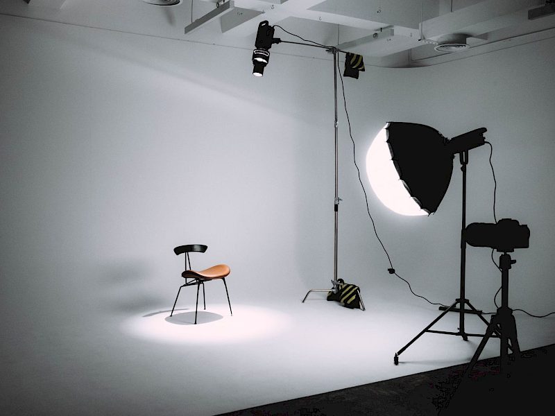 Helles Fotostudio mit Softbox, Kamera auf Stativ und einem Stuhl vor weißer Hohlkehle