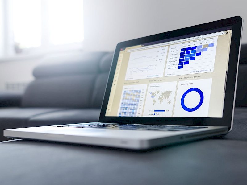 Laptop mit geöffnetem Dashboard voller Diagramme auf einem grauen Sofa