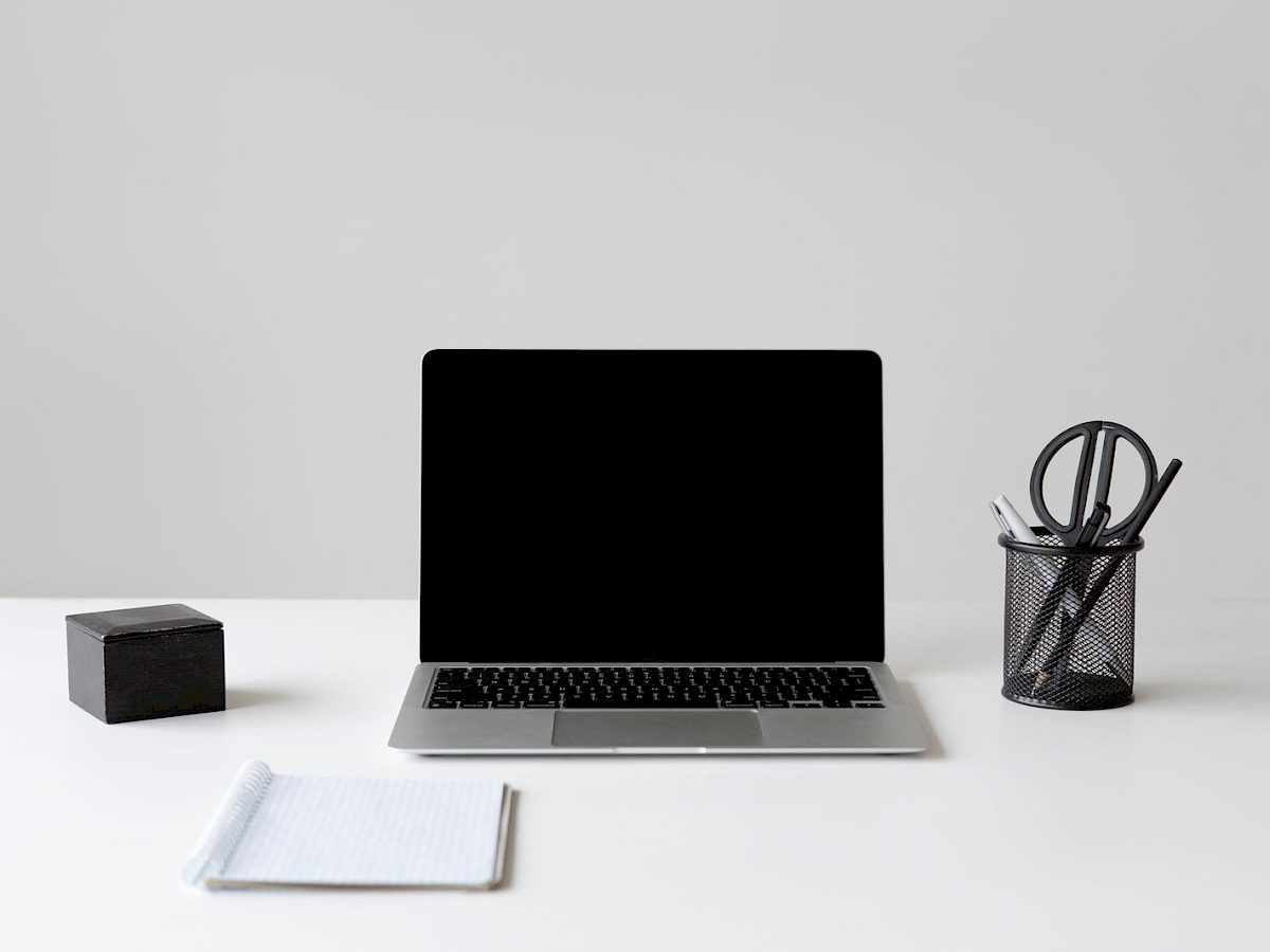 Minimalistischer Arbeitsplatz mit Laptop, Notizblock und Stiftehalter auf einem weißen Tisch
